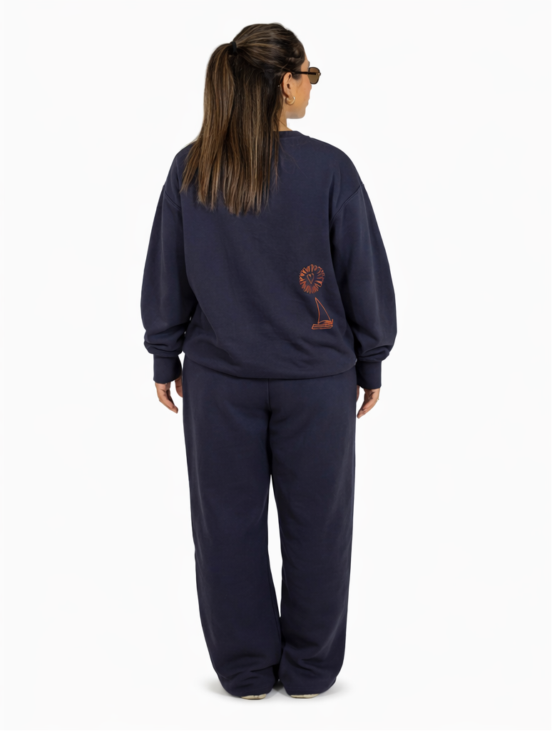 Woman wearing a navy blue tracksuit with orange designs, holding a drink and a green bag.