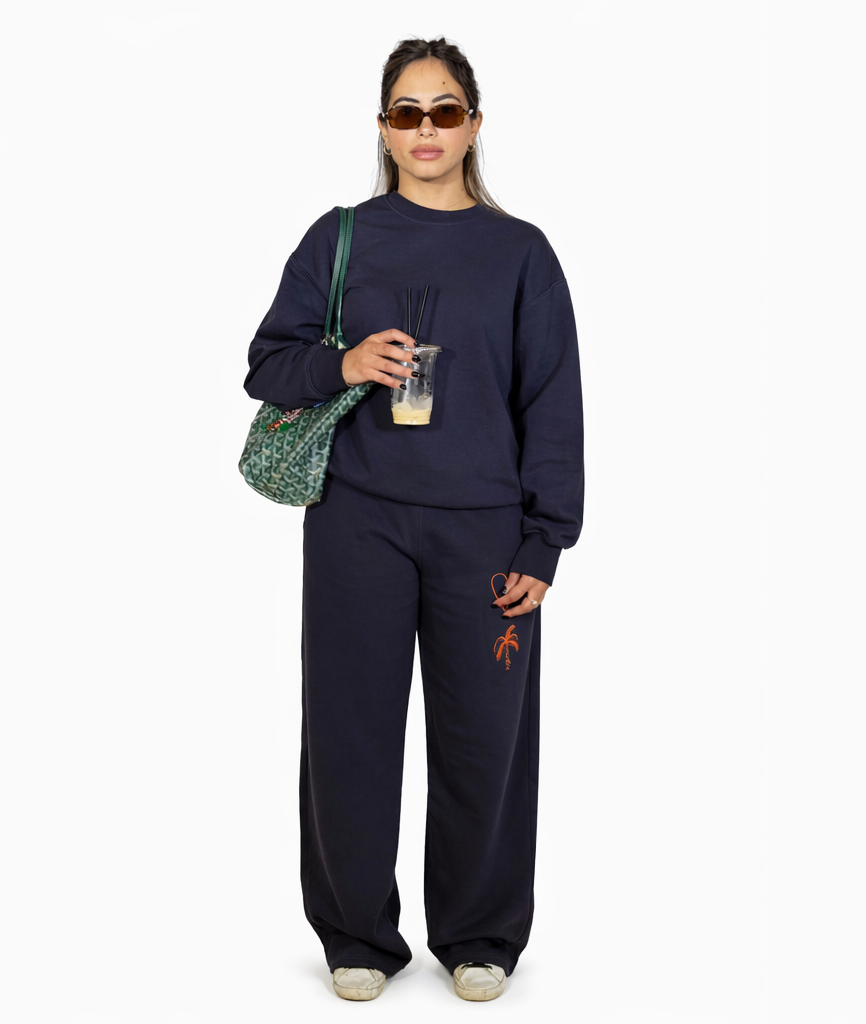 Woman wearing a navy blue tracksuit with orange designs, holding a drink and a green bag.